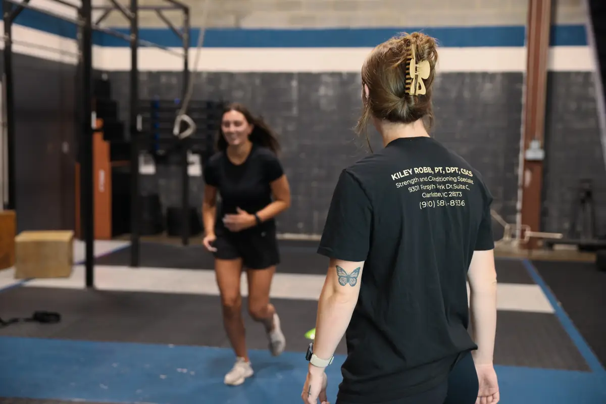 An athlete runs a cone agility drill while Dr. Kiley coaches her in the gym