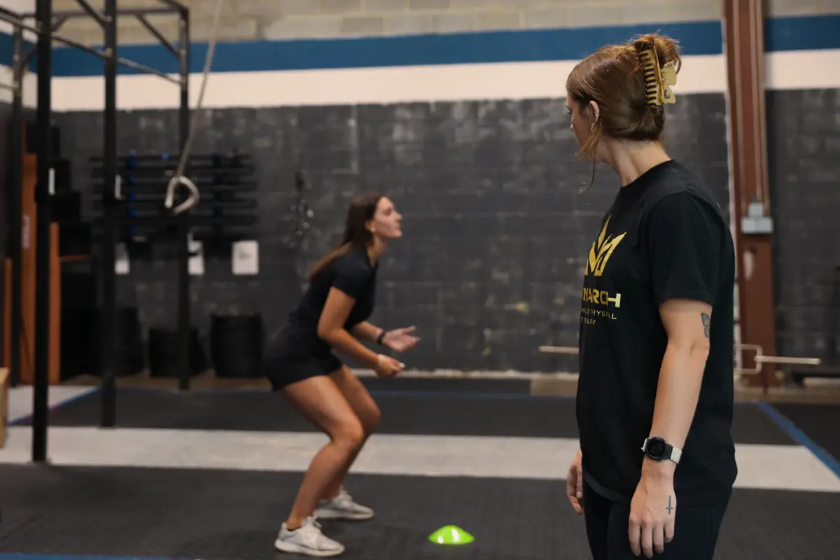 An athlete holds a ready stance at a cone while Dr. Kiley watches
