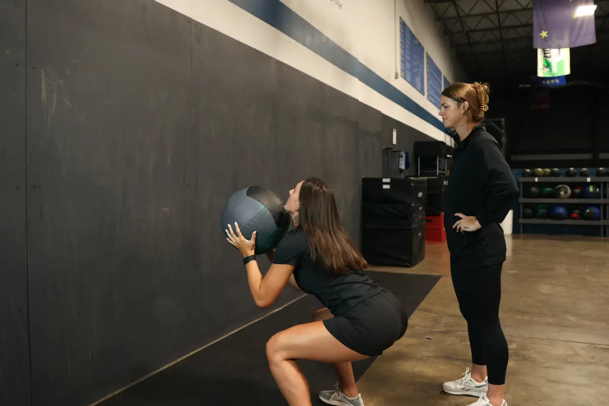 An athlete squats with a wall ball while Dr. Kiley coaches her